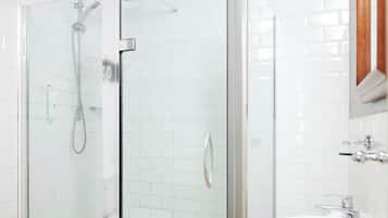 A bathroom with a glass-enclosed shower, white tiled walls, and a white sink with chrome fixtures.