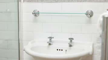 A bathroom with a white sink, two faucets, and a glass shelf above the sink.