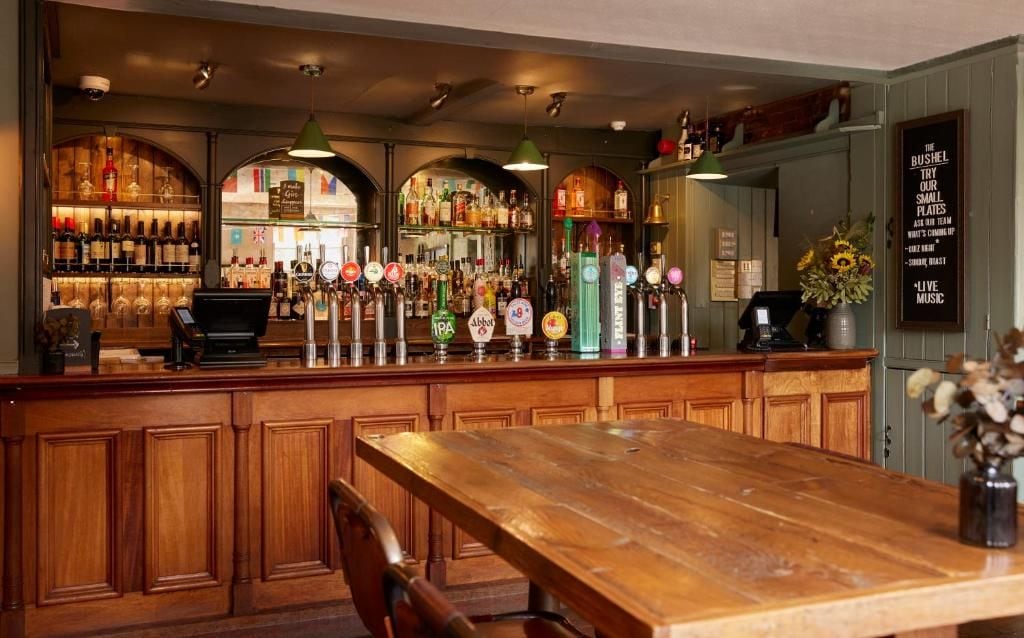 Angolo bar con un bancone in legno, diverse spine e una varietà di bottiglie.