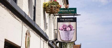 A street sign for 'The Bushel' and 'Greene King' on a building facade.