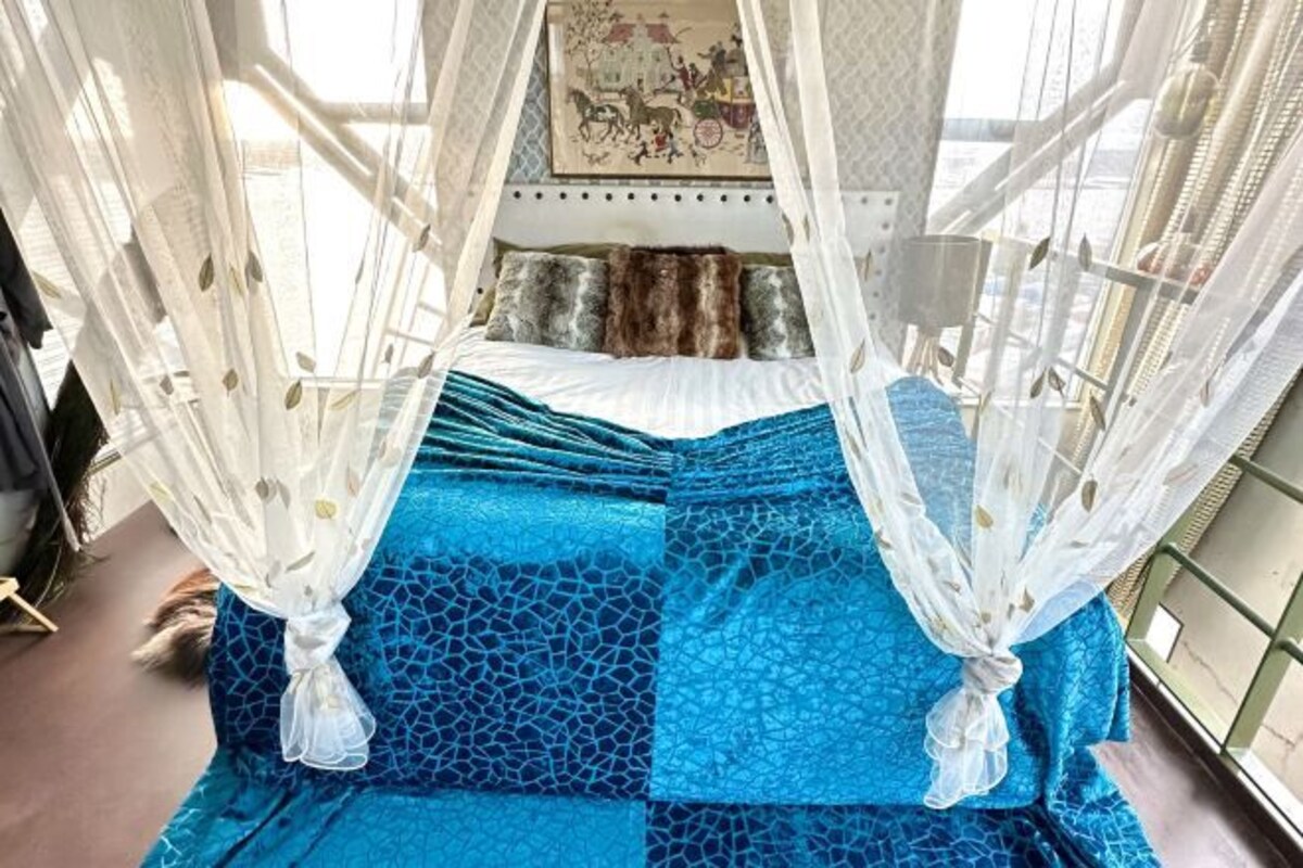 A bed with a blue patterned bedspread, white canopy, and a painting above it.