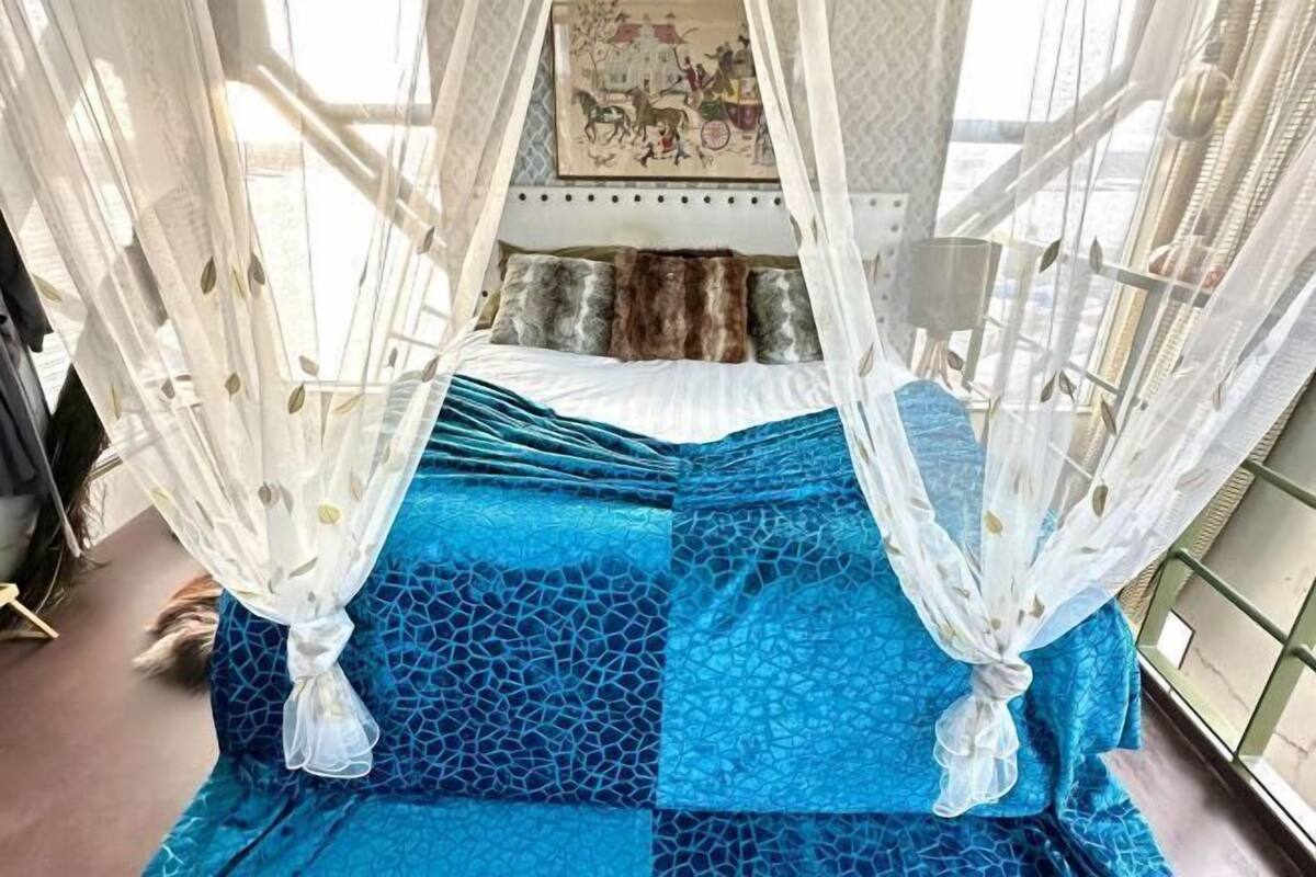 Een bed met een blauw beddegoed met een patroon, een wit baldakijn en een schilderij erboven.