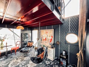 Een kamer met een hangstoel, een bureau met een vaas, een schilderij en een boekenkast.