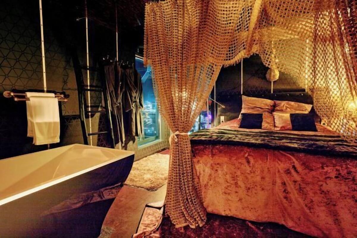 Een kamer met een groot bad, een bed met hemelbed en een hangstoel.