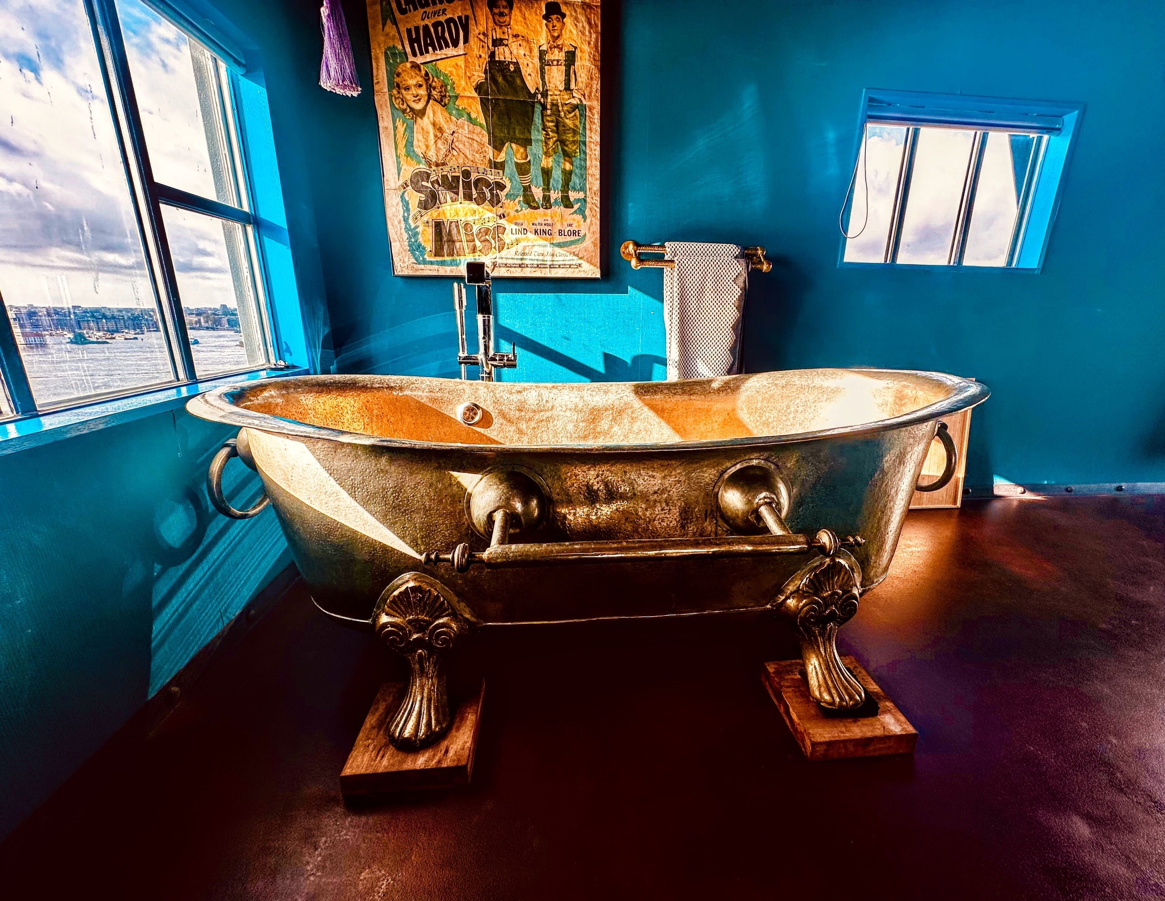 Eine Badewanne mit Pfotenfüßen im Vintage-Stil in einem Raum mit großen Fenstern und einem Poster an der Wand.