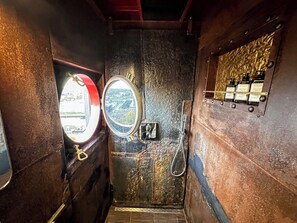 Een smalle gang met een deur, een ronde spiegel en een raam met rode omlijsting.