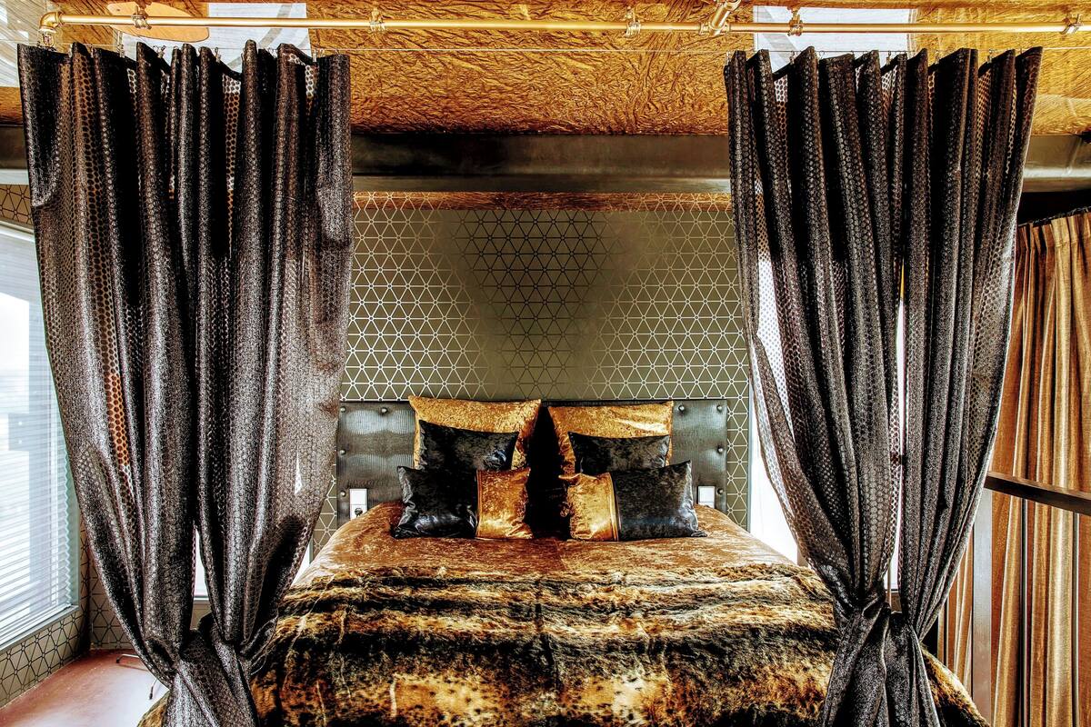 Een bed met een bedsprei met patroon, een hoofdbord en gordijnen.