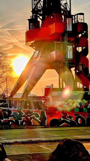 Een groot industrieel gebouw met graffiti, een ondergaande zon op de achtergrond en een grasveld vooraan.