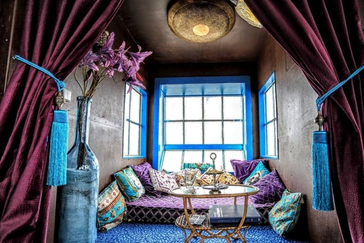 Een knus vertrek met een blauw raam, een ronde tafel en een comfortabele zithoek.