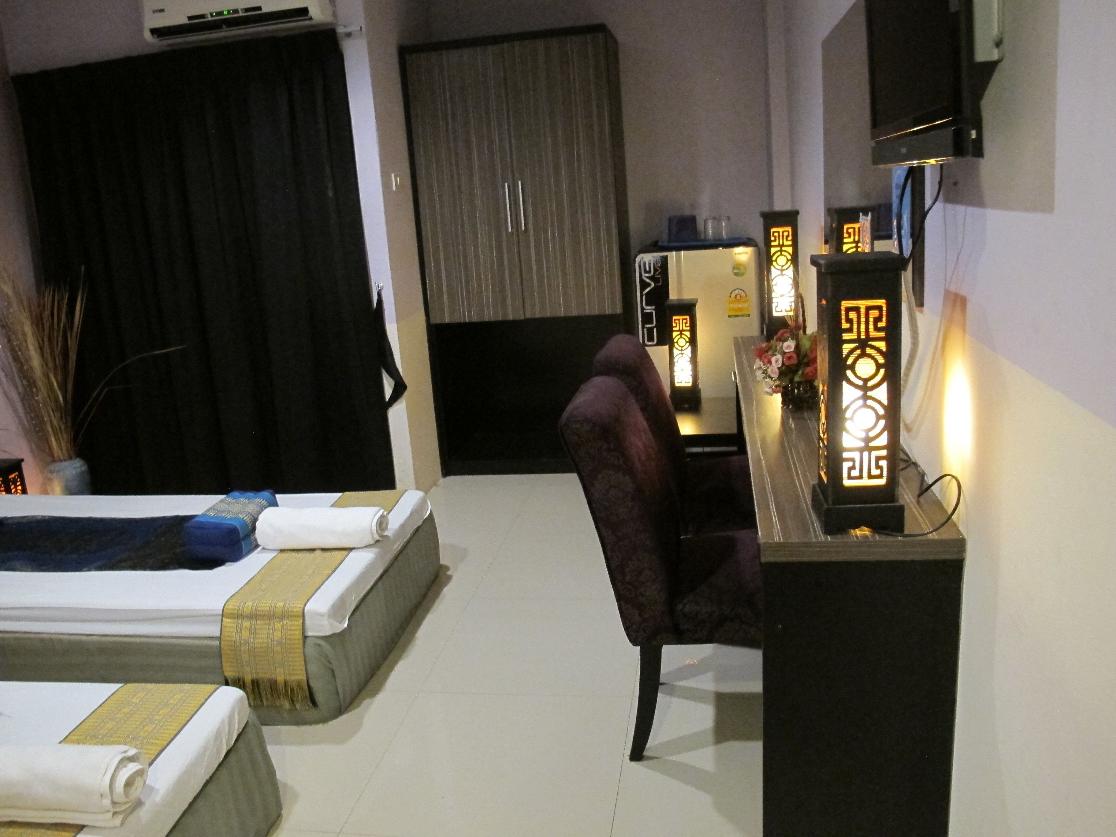 A hotel room with a bed, a chair, a desk with a lamp, and a TV.