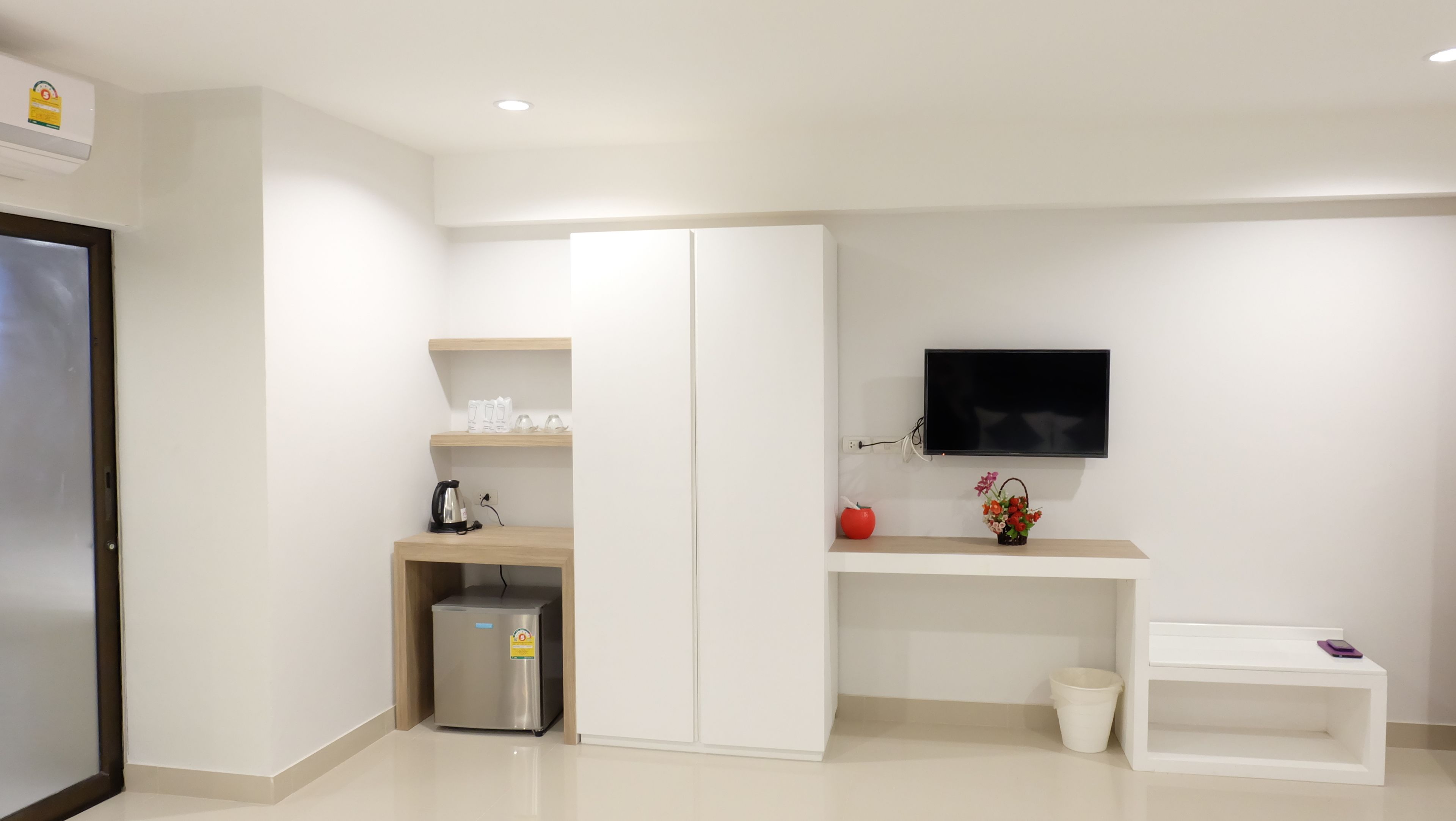 A modern kitchen with white cabinetry, a built-in fridge, a coffee maker, and a TV mounted on the wall.