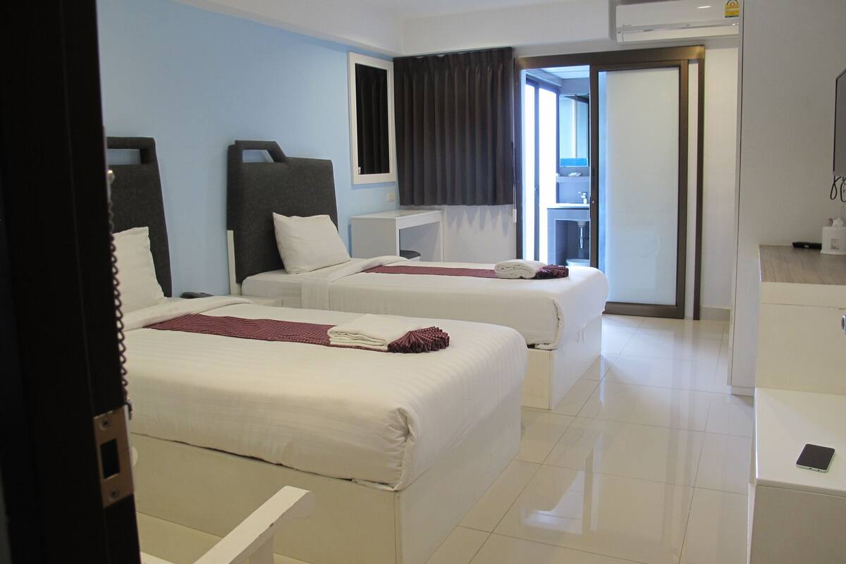 A hotel room with two beds, a desk, a mirror, and a bathroom visible through an open door.