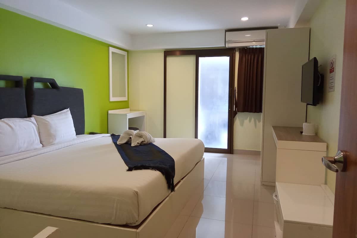 A hotel room with a large bed, a bedside table, a mirror, a TV, and a sliding door leading to a balcony.