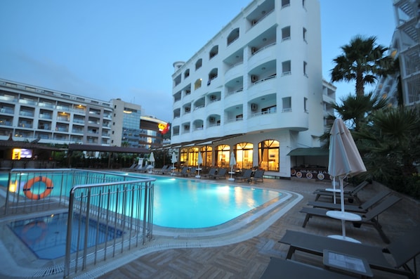 A hotel pool area with a clear pool, lounge chairs, and a snack bar.
