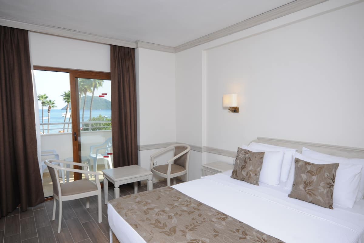 A hotel room with a bed, a chair, a small table, and a view of the ocean through a glass door.