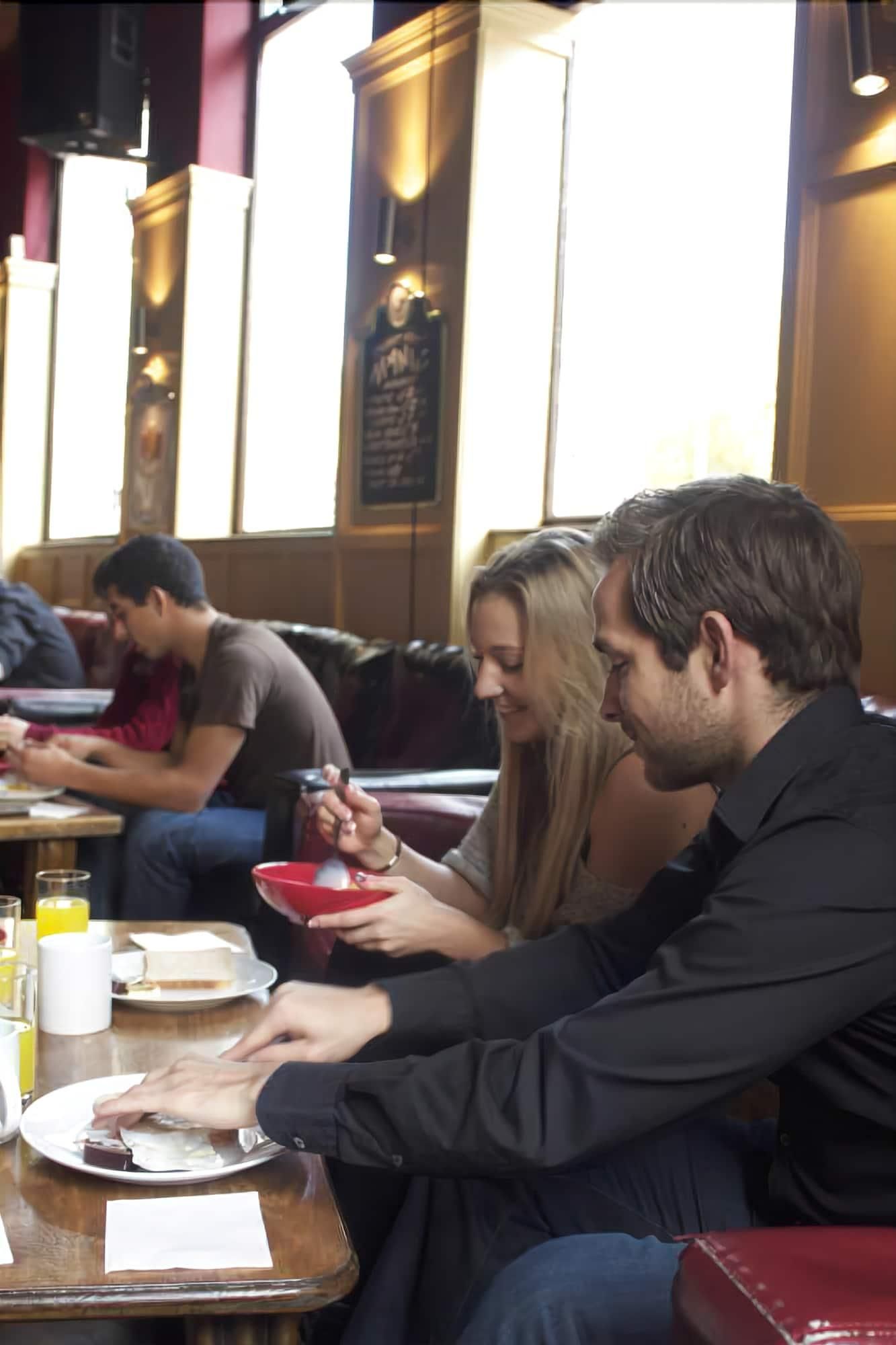 A group of people dining at a restaurant with a high ceiling and large windows.