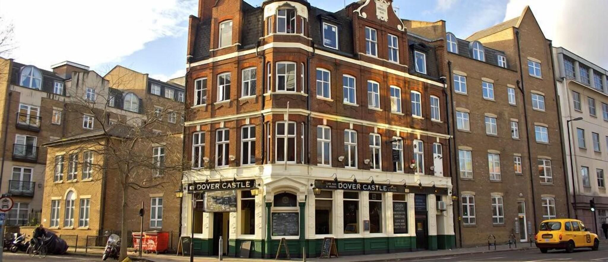 A multi-story building with a prominent corner entrance, a sign reading 'DOVER CASTLE,' and a yellow taxi parked in front.