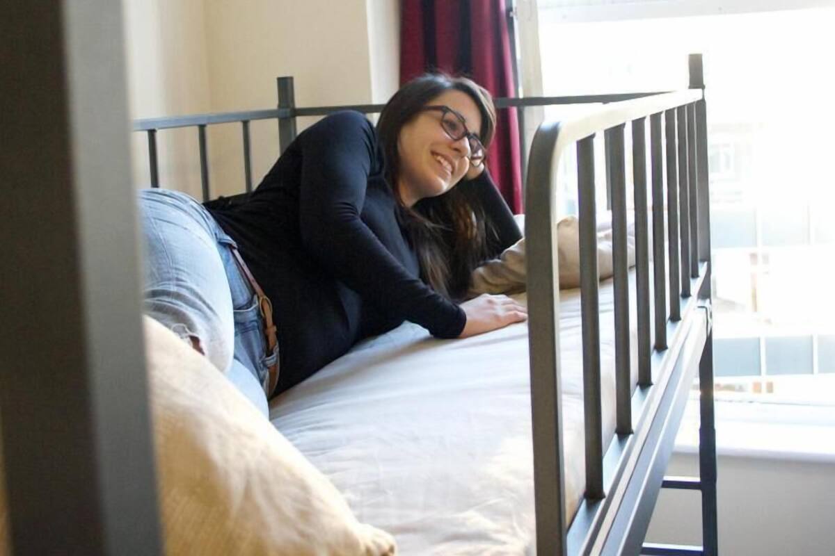 A person lying on a bed in a room with a window and a metal railing.