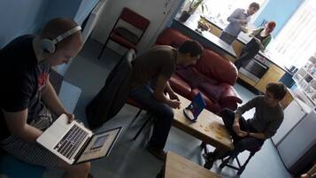 A room with a red couch, a wooden table, and a laptop on a chair.