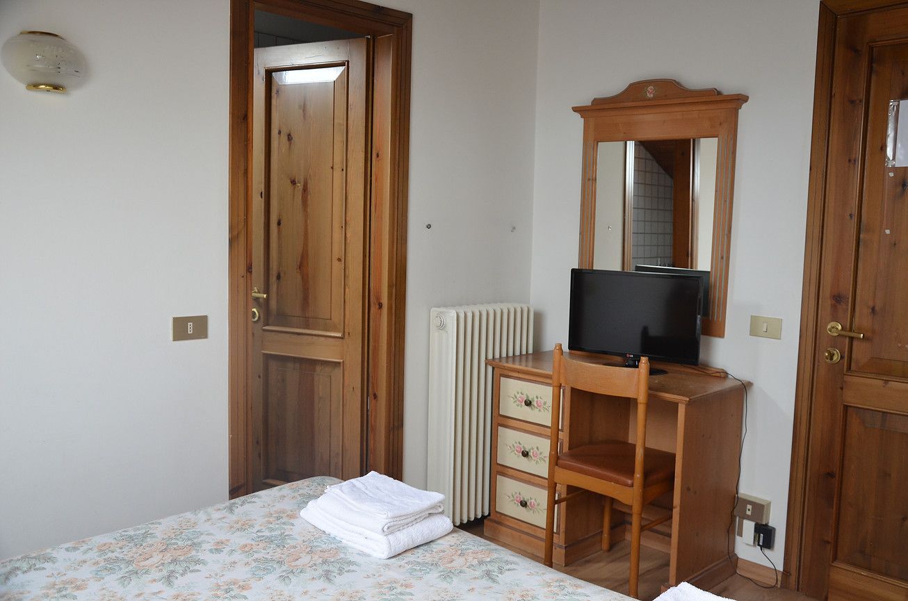 Una camera da letto con un letto, una cassettiera in legno con specchio, un termosifone e una televisione.
