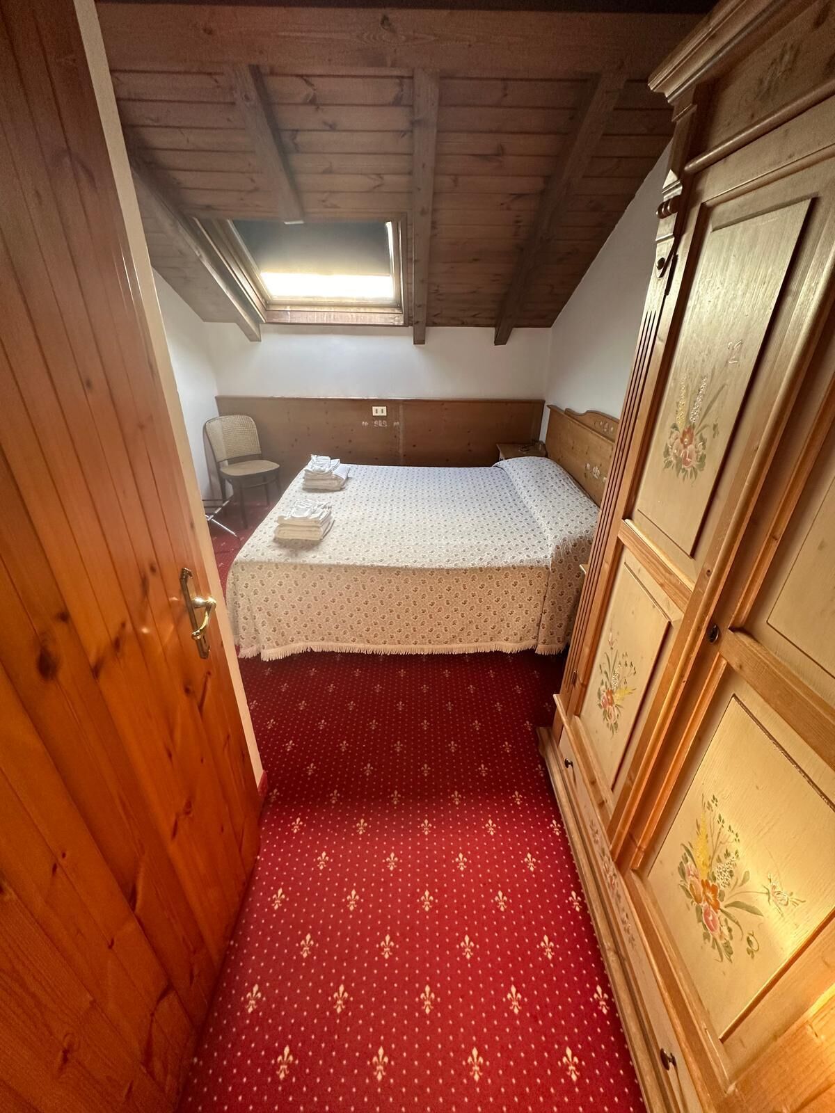 A small, cozy room with a wooden ceiling, a single bed, a chair, and a dresser.