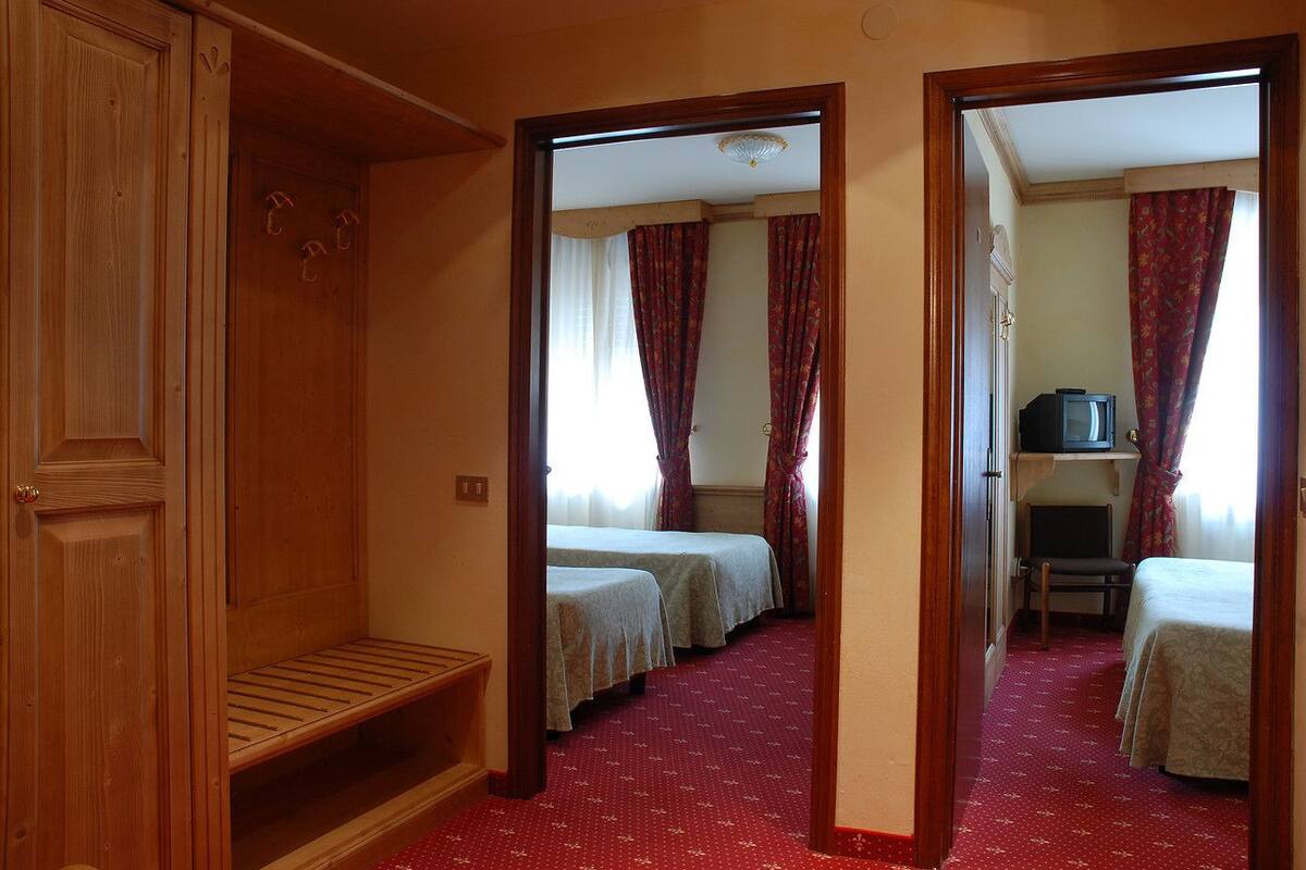 A hotel room with two single beds, a wooden wardrobe, a television, and a small desk.