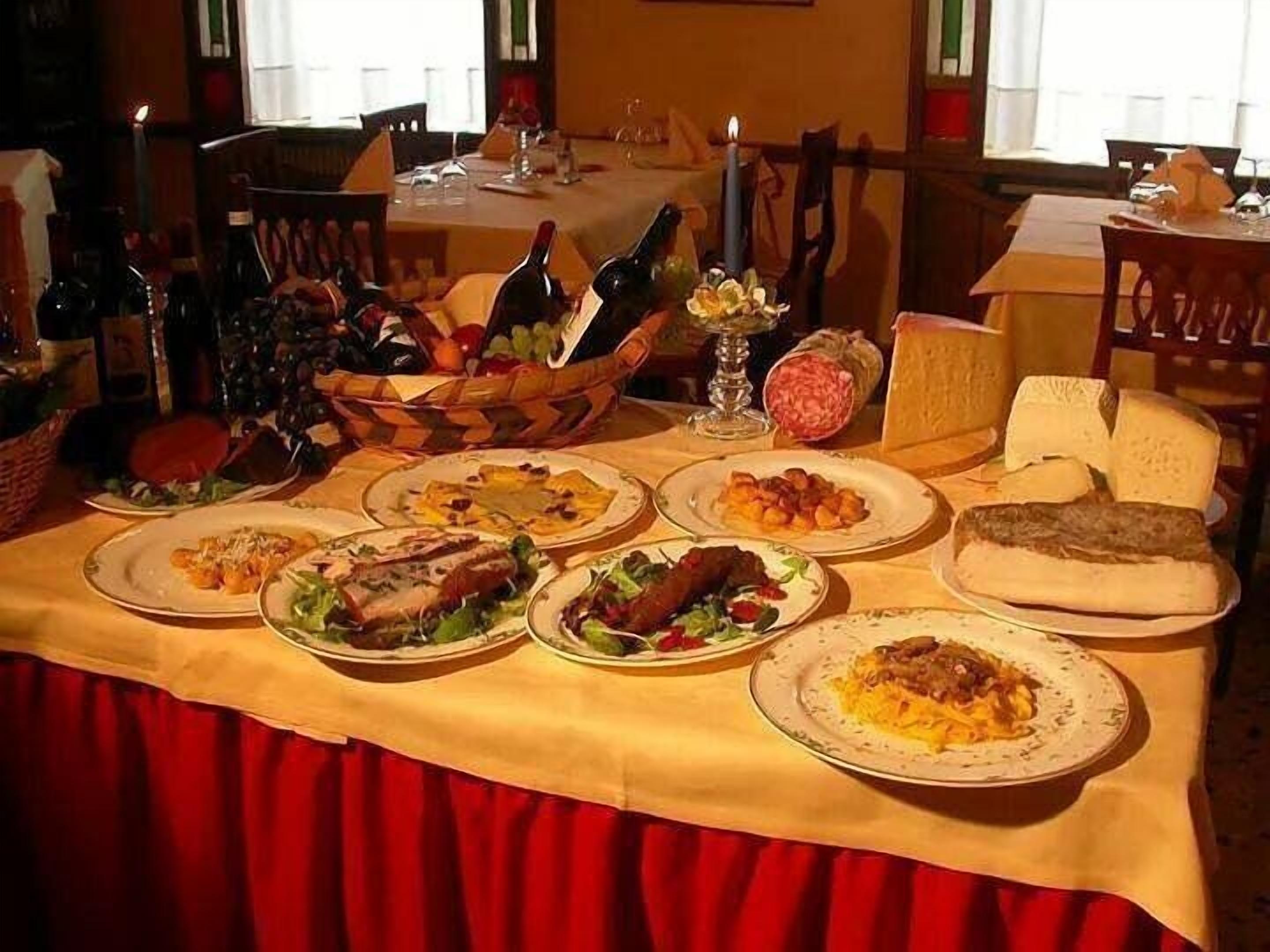 Une table à manger dressée avec divers plats, notamment des pâtes, de la viande et du pain, dans une pièce aux rideaux rouges et aux meubles en bois.