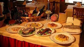 Une table à manger dressée avec divers plats, notamment des pâtes, de la viande et du pain, dans une pièce aux rideaux rouges et aux meubles en bois.