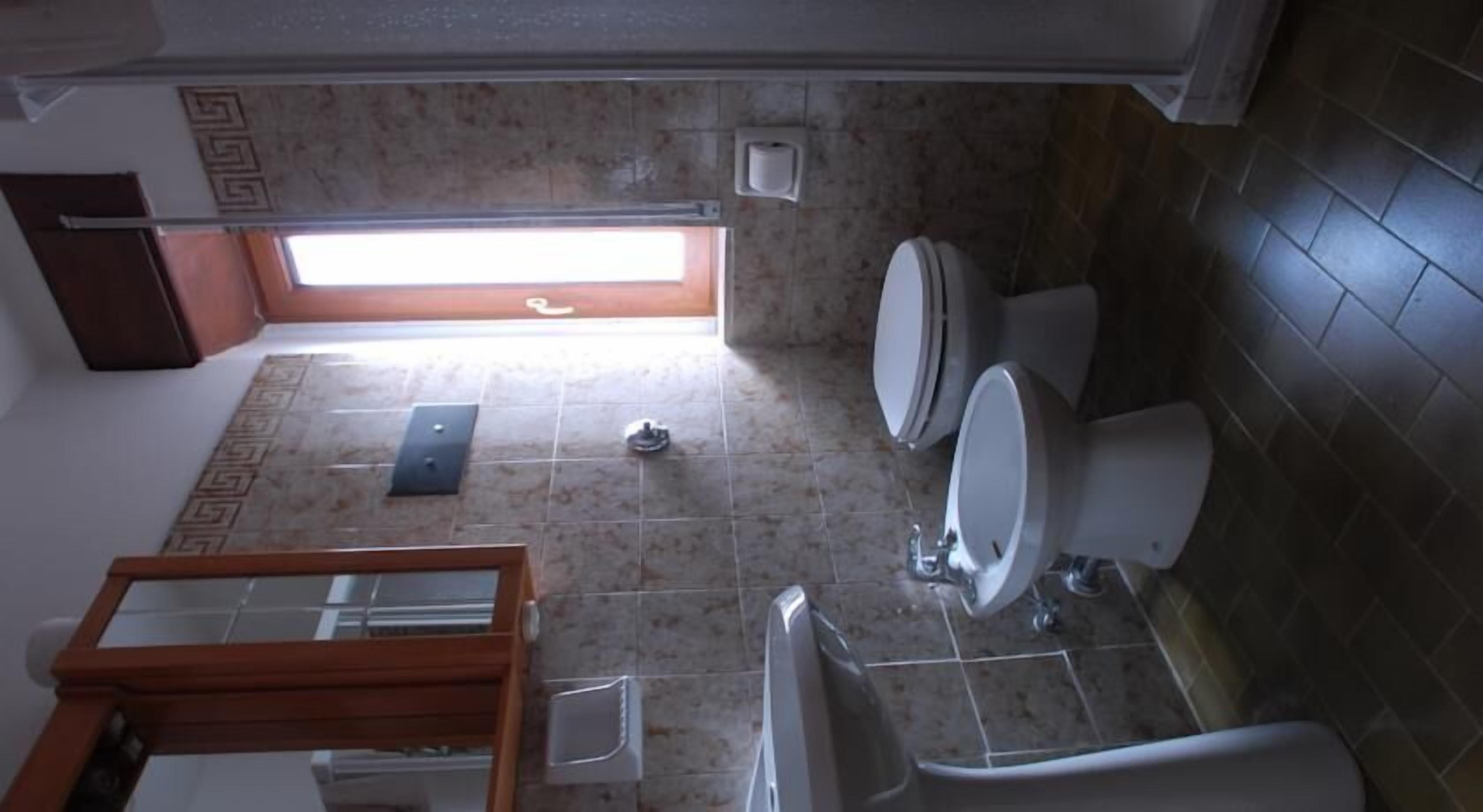 A bathroom with two toilets, a sink, and a bathtub. There is a window providing natural light.
