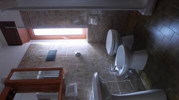 A bathroom with two toilets, a sink, and a bathtub. There is a window providing natural light.