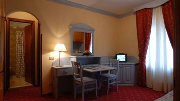 A hotel room with a dining table, two chairs, a television, a mirror, and a red carpet.