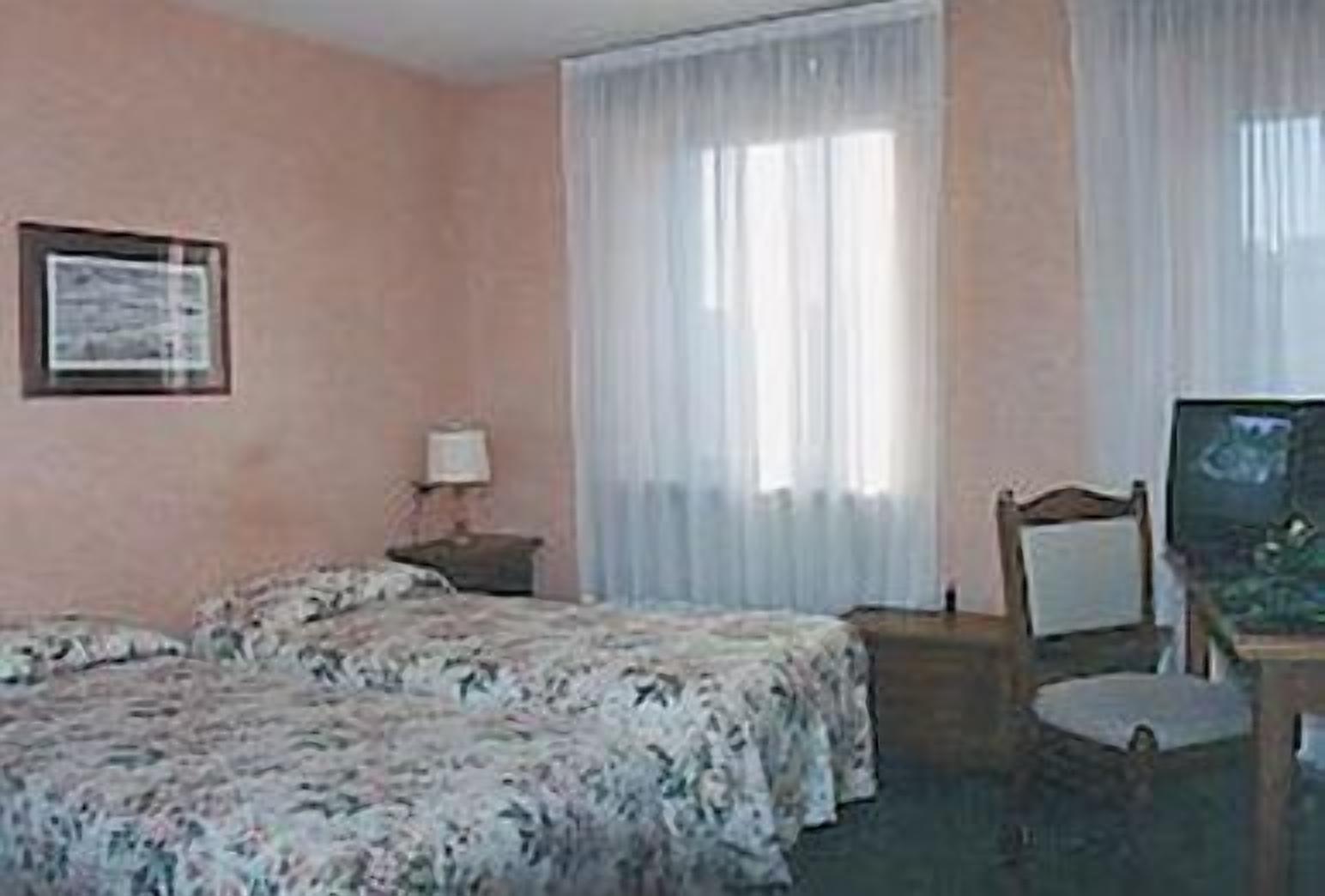 A hotel room with two beds, a desk with a chair, a television, and a window with sheer curtains.