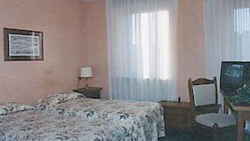 A hotel room with two beds, a desk with a chair, a television, and a window with sheer curtains.