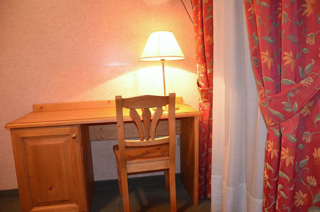Una scrivania in legno con una sedia, una lampada e una tenda floreale.