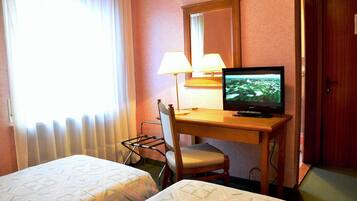 Une chambre d’hôtel avec un lit, un bureau avec une télévision, une chaise et une fenêtre avec des rideaux.