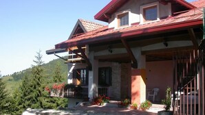 Una casa de dos pisos con techo rojo, un balcón y cimientos de piedra.
