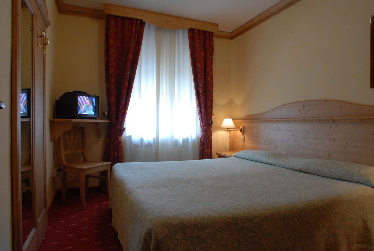 Ein Hotelzimmer mit Bett, Stuhl, Fernseher und einem Fenster mit Vorhängen.