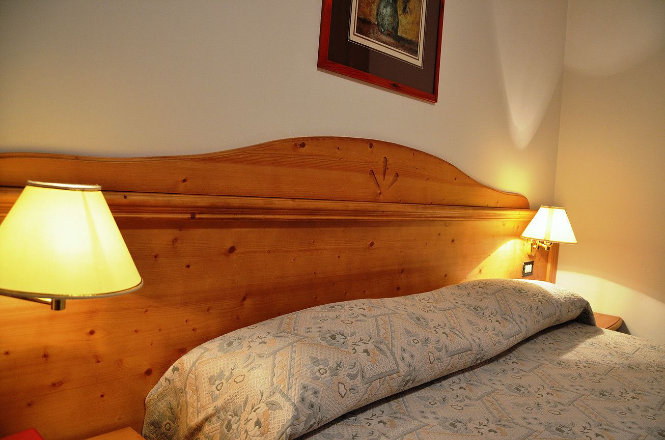 Un dormitorio con cabecera de madera, dos lámparas de noche, un edredón estampado y un cuadro en la pared.