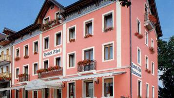 Ein pinkfarbenes Gebäude mit mehreren Fenstern und Balkonen, mit der Aufschrift "Hotel Alpen".