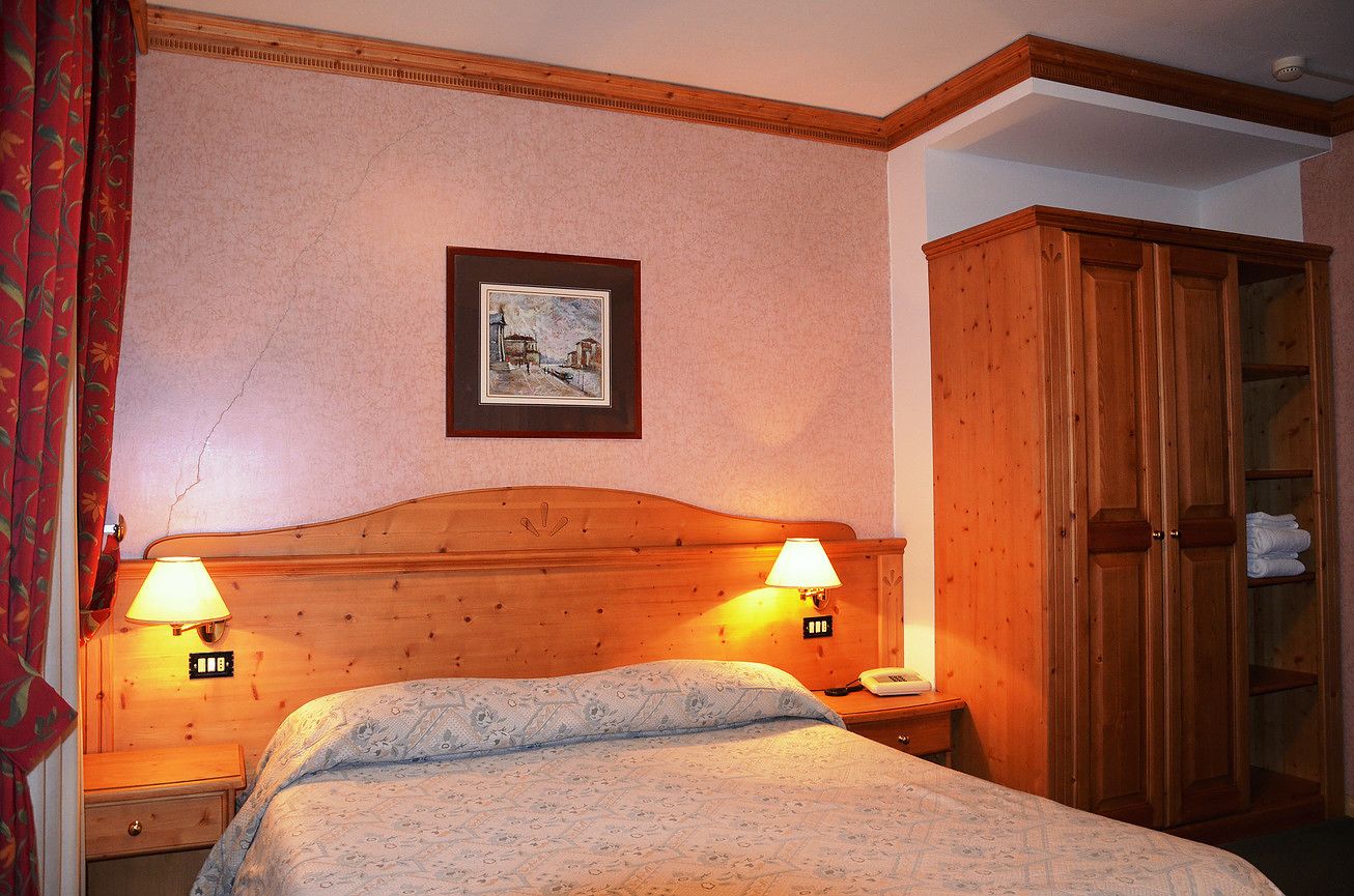 Un dormitorio con cabecera de madera, dos lámparas de noche, un cuadro enmarcado en la pared y un armario de madera.