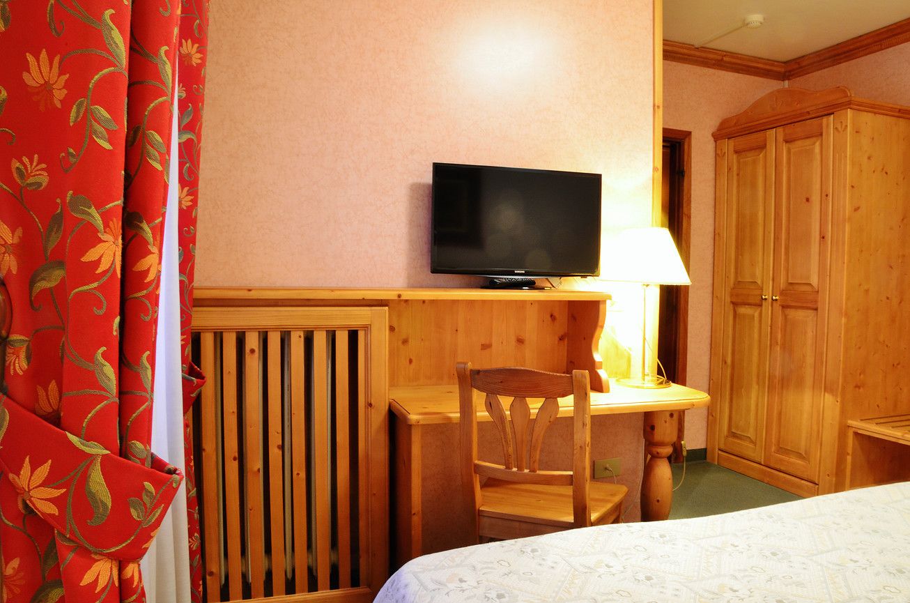 A hotel room with a bed, a wooden desk with a television, a chair, and a wardrobe.