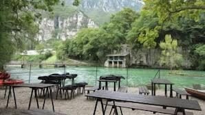 Un restaurante a la orilla del río con terraza y vistas al río y la vegetación circundante.