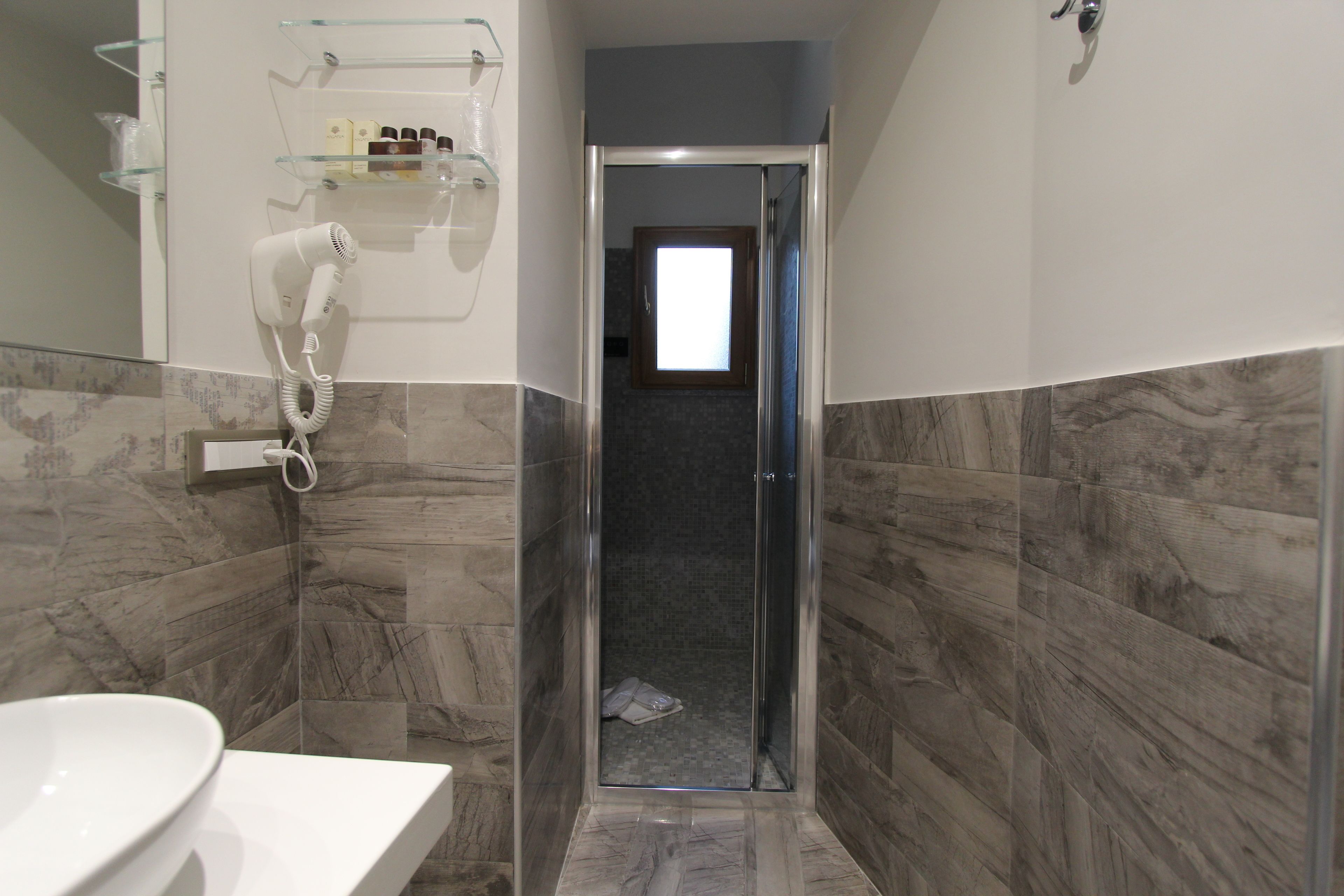 A bathroom with a white sink, a glass shower enclosure, and a marble-tiled wall.