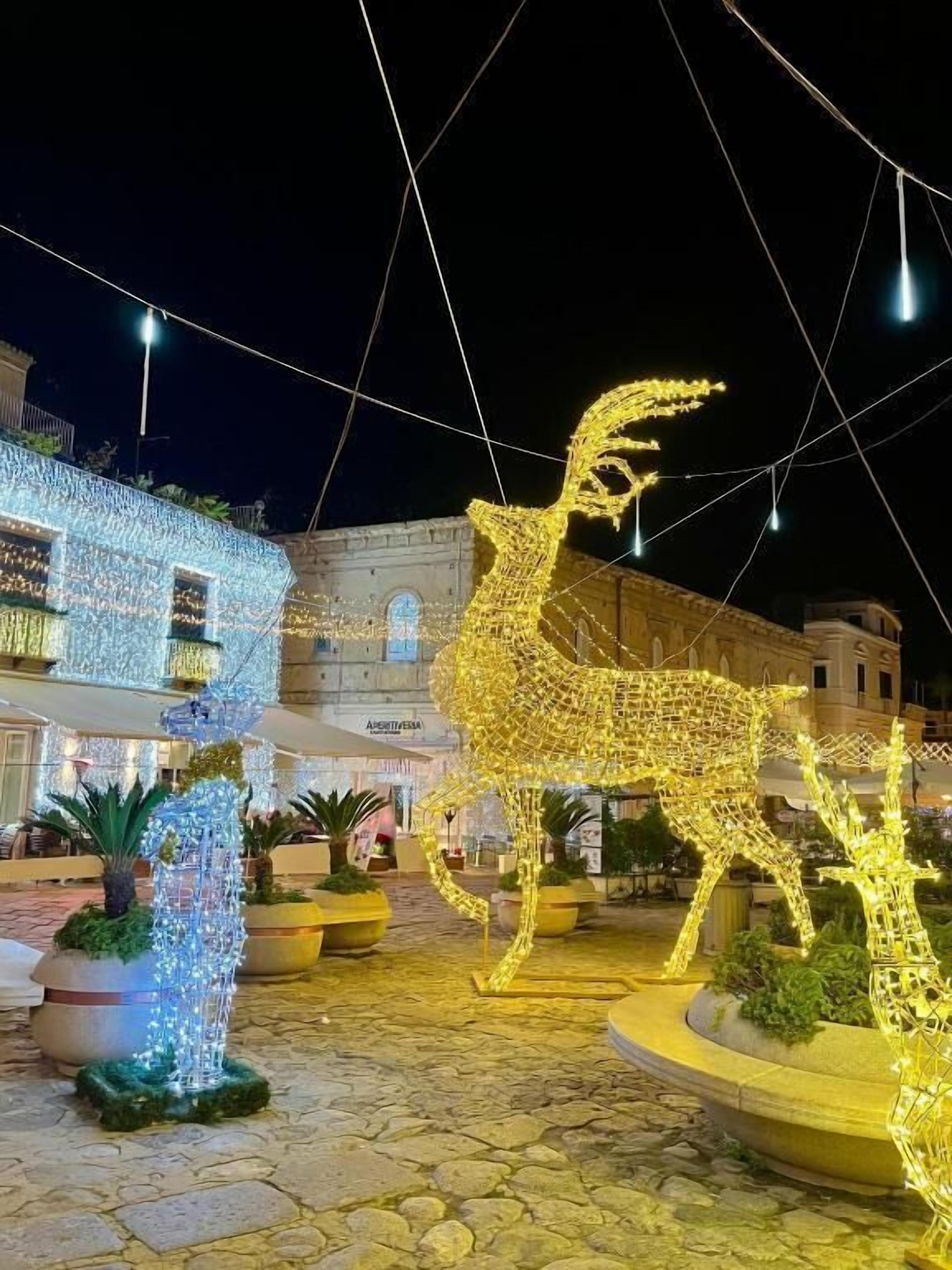 Un patio con una gran escultura iluminada de ciervo, plantas en macetas y un edificio con luces.
