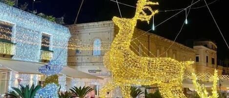 Un patio con una gran escultura iluminada de ciervo, plantas en macetas y un edificio con luces.