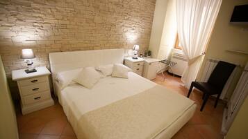 Un dormitorio con pared de ladrillo, una cama con cabecera, dos mesitas de noche con lámparas, una silla y un radiador.