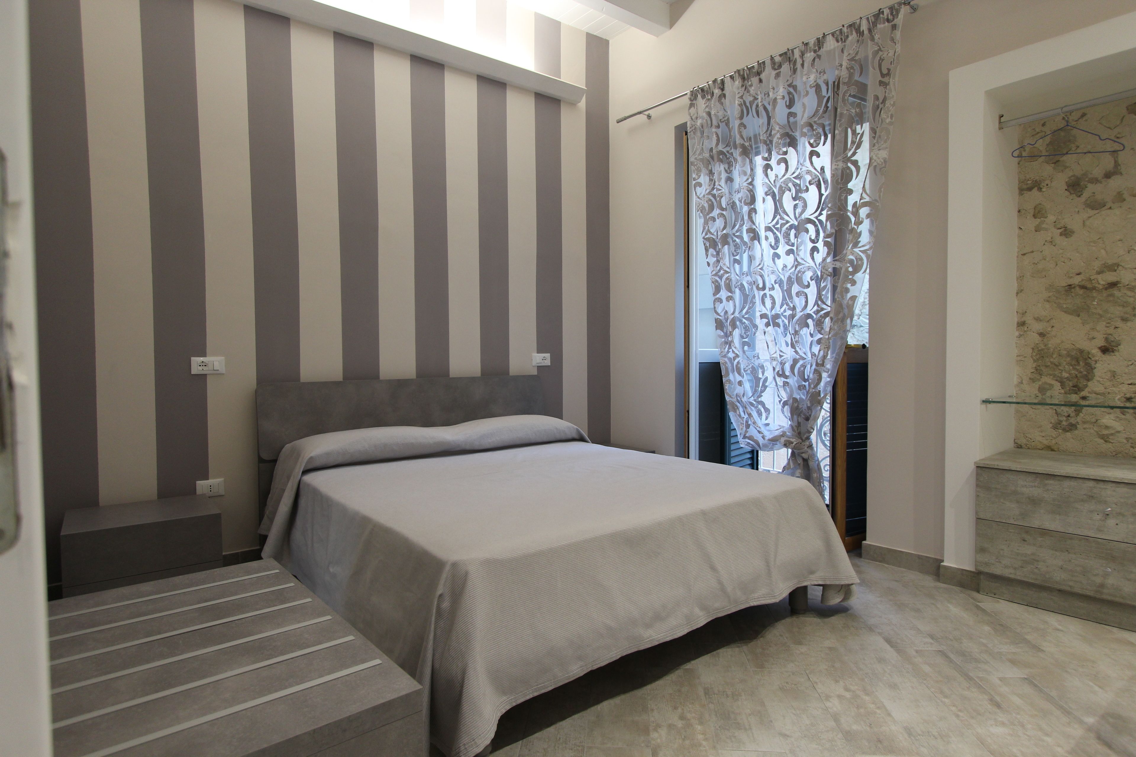 A bedroom with a bed, a headboard, a window with curtains, and a staircase.
