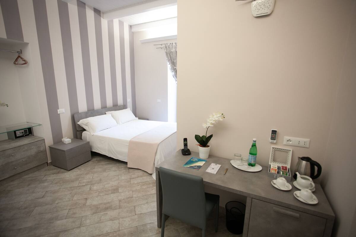 Une chambre d’hôtel comprenant un lit, une table de chevet, un bureau avec un service à thé et une plante en pot.