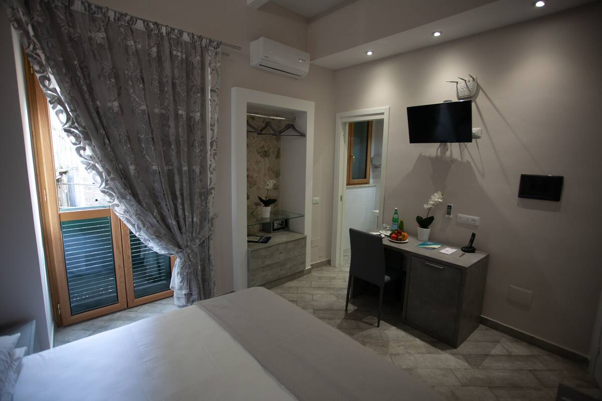 Une chambre à coucher comprenant un lit, un bureau, une chaise, un téléviseur et une salle de bain visible à travers une porte.