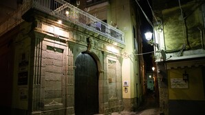 A narrow street with a building featuring a large black door and a balcony with ornate metal railings. - Residenza Le due Sicilie (Tropea)